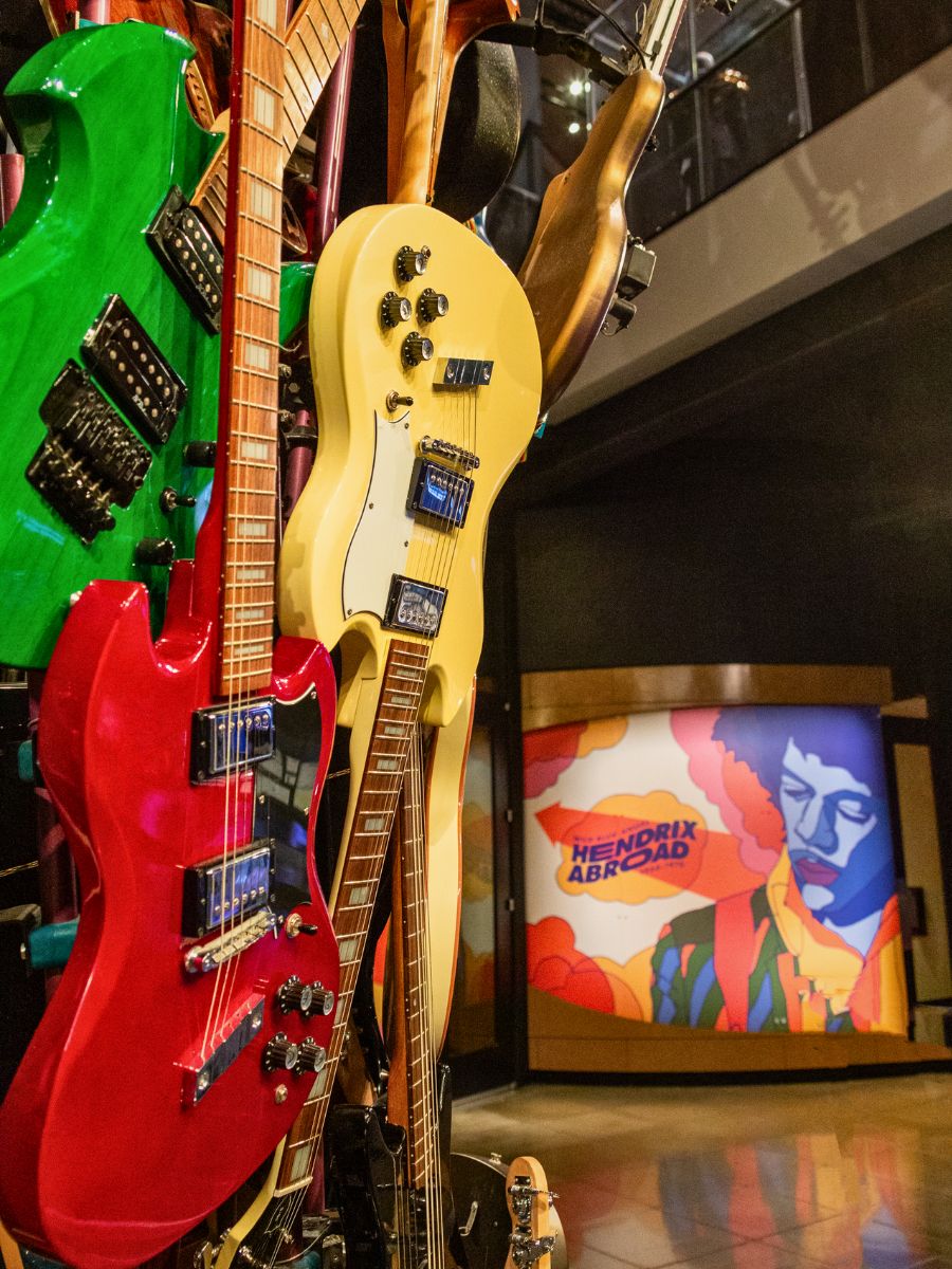A display of colorful electric guitars is showcased in a museum, with a "Hendrix Abroad" exhibit in the background.