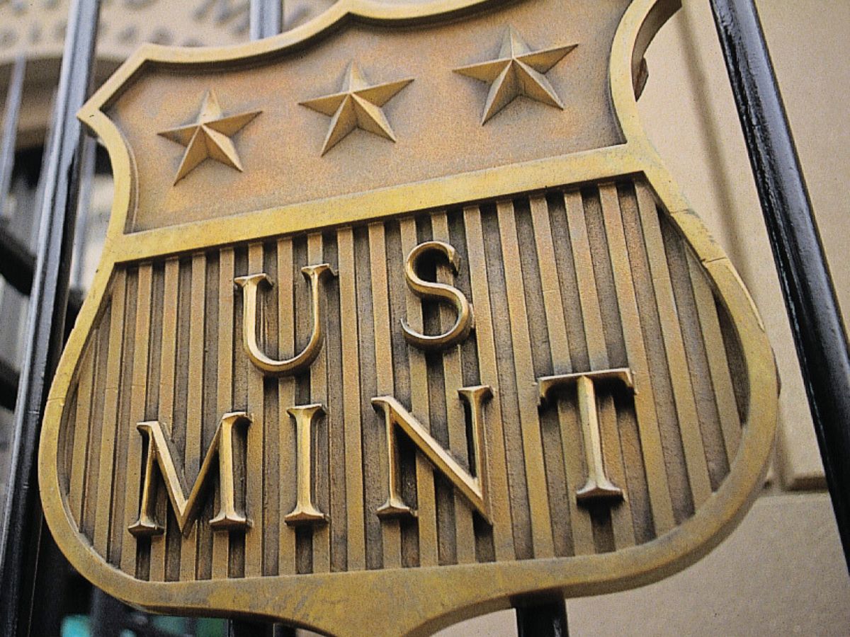 Bronze plaque reading "US Mint" with three stars above, mounted on a gate.