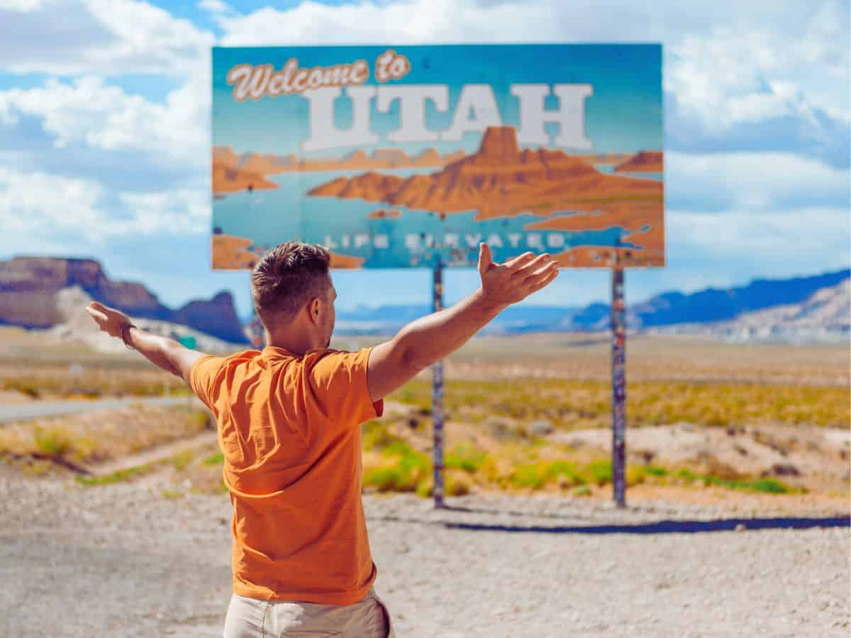 A man excitedly standing in front of a welcome to Utah sign, looking forward to discovering all the things to do in Utah.