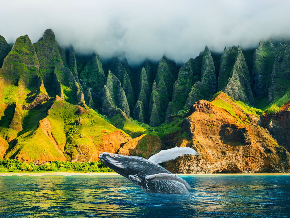 A whale breaches near a lush, mountainous coastline with jagged peaks and cloud cover.