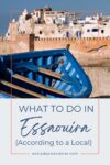 Blue wooden boat in front of a beige historic building under a clear sky, with text overlay: "What to do in Essaouira (According to a Local)" and the website everydaywanderer.com.