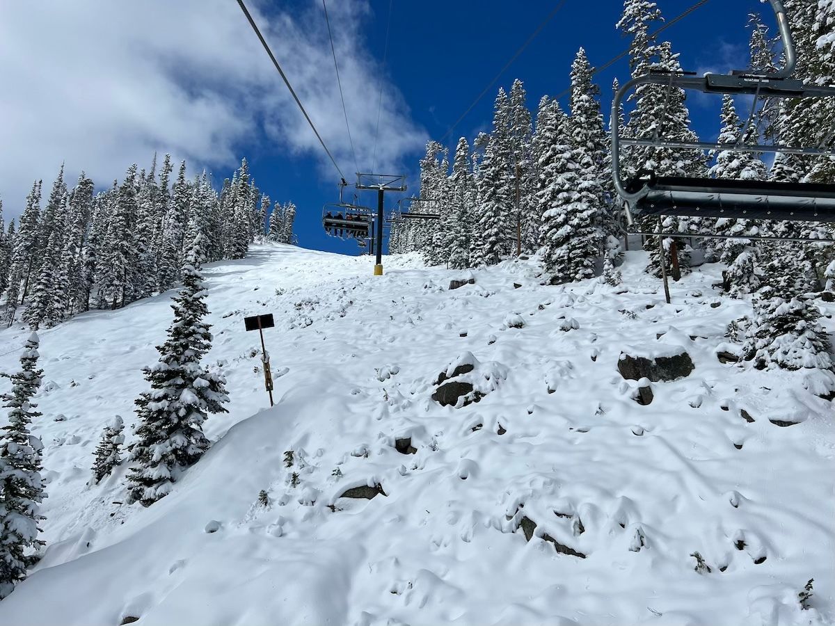 Ski lift ascending a snowy mountain slope surrounded by snow-covered trees under a blue sky.