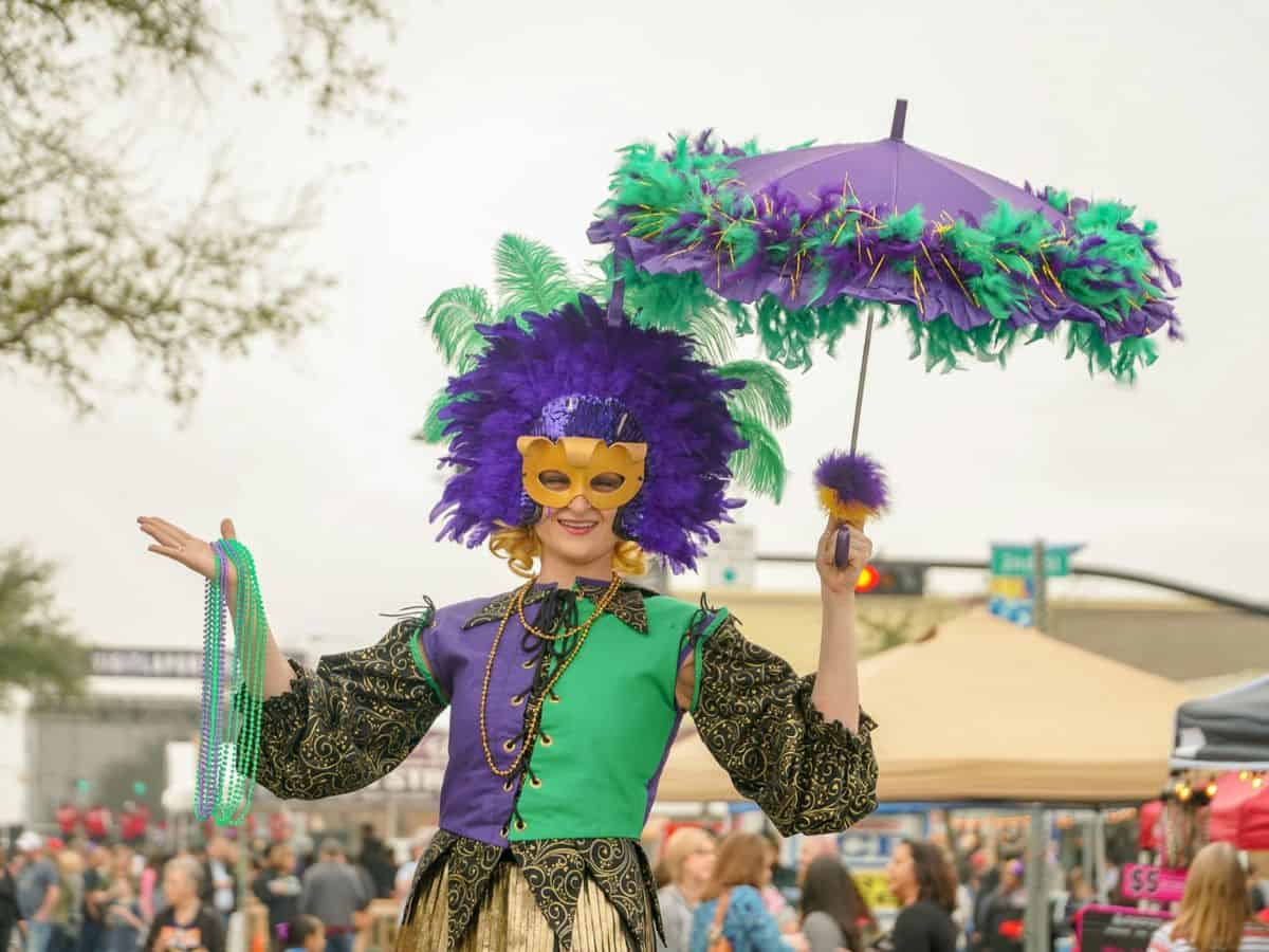 A woman in a mardi gras costume holding an umbrella.