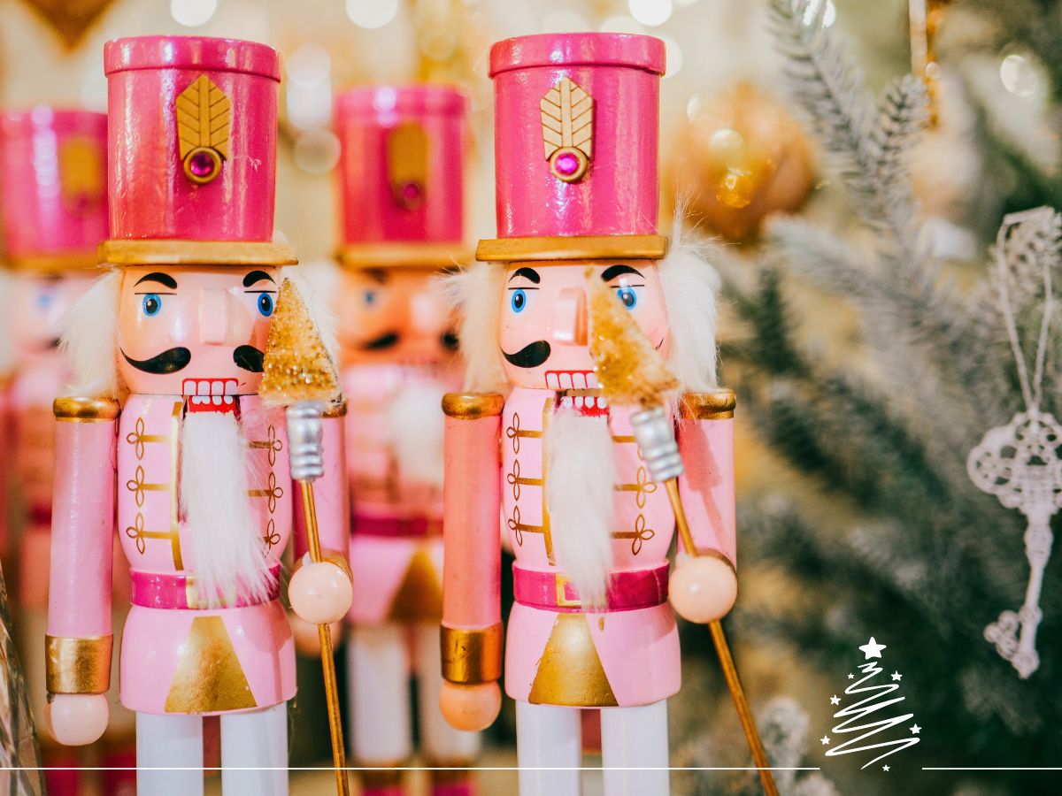 A group of pink wooden nutcracker figurines with gold accents stand in front of a decorated Christmas tree.